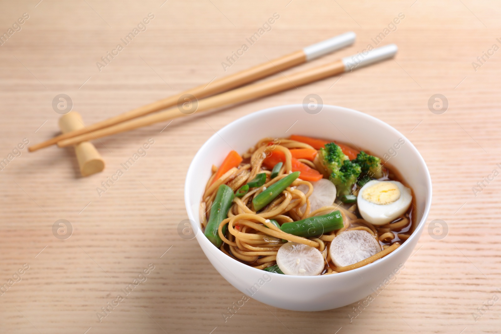 Photo of Tasty ramen with noodles and vegetables on wooden table