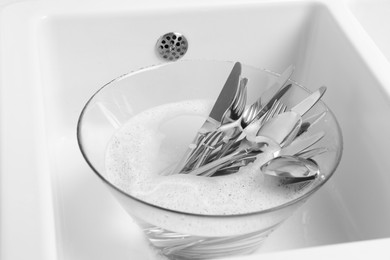 Photo of Washing silver spoons, forks and knives in kitchen sink