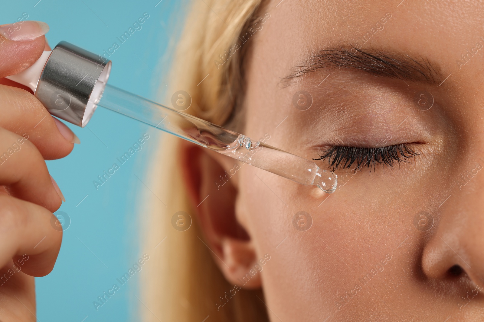 Photo of Woman applying cosmetic serum onto her face on light blue background, closeup