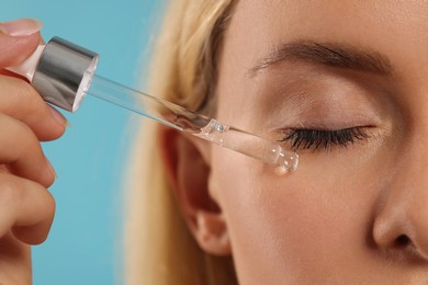 Photo of Woman applying cosmetic serum onto her face on light blue background, closeup