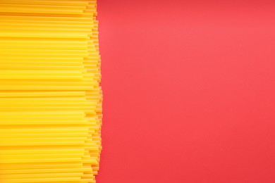 Yellow plastic drinking straws on red background, flat lay. Space for text