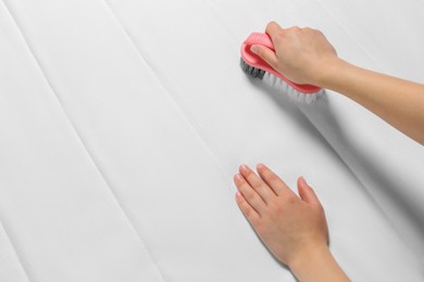 Photo of Woman cleaning white mattress with brush, closeup. Space for text