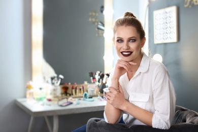 Photo of Beautiful young woman with makeup made by professional artist in dressing room