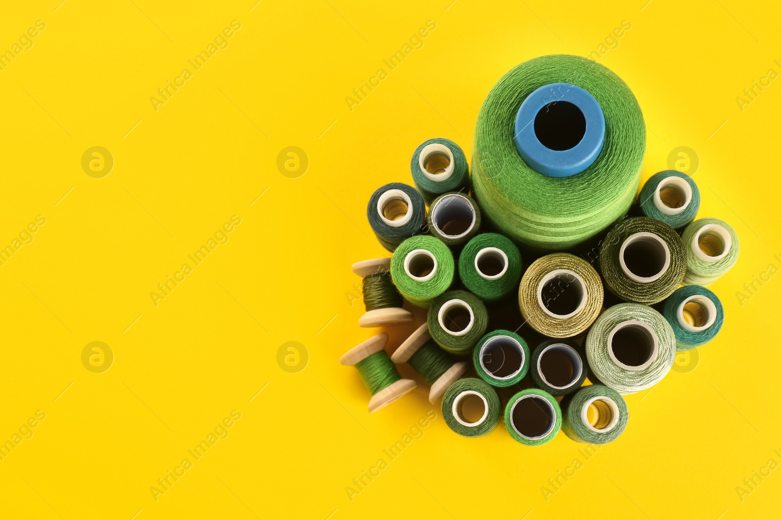 Photo of Different shades of green sewing threads on yellow background, flat lay. Space for text