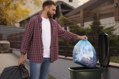 Photo of Man putting garbage bag into recycling bin outdoors