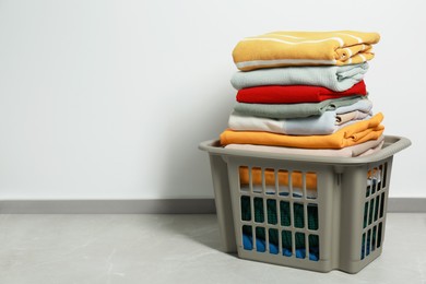 Photo of Plastic laundry basket with clean clothes on floor indoors, space for text
