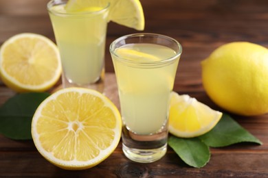 Photo of Tasty limoncello liqueur, lemons and green leaves on wooden table, closeup