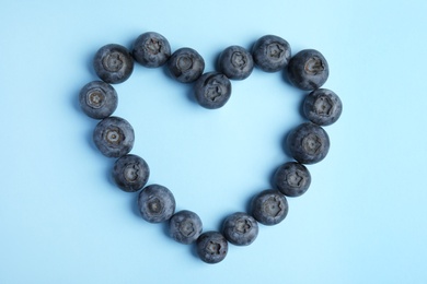 Heart shaped frame of blueberries on blue background, flat lay with space for text