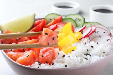 Taking piece of salmon from tasty poke bowl with chopsticks on table, closeup