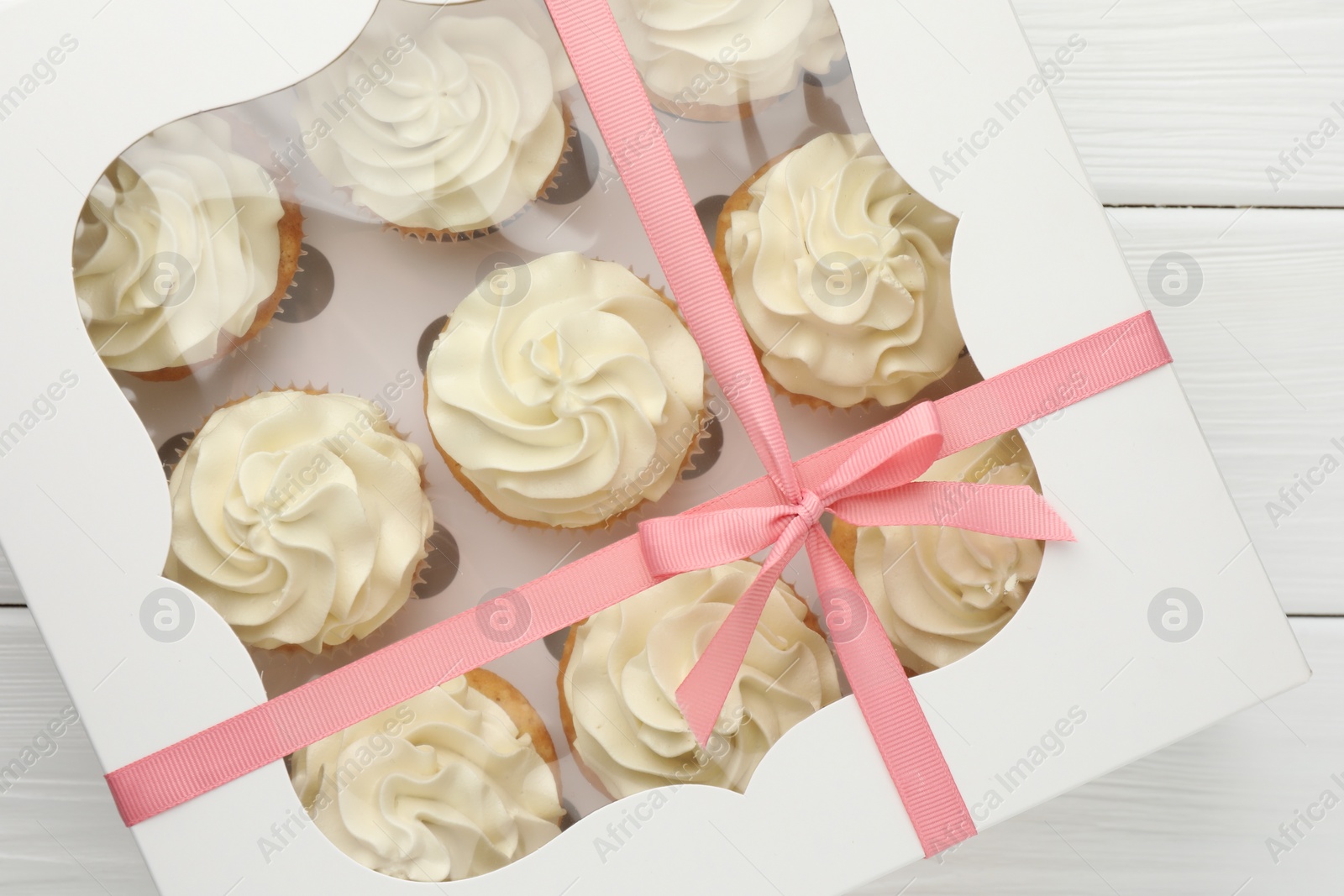 Photo of Tasty cupcakes with vanilla cream in box on white wooden table, top view