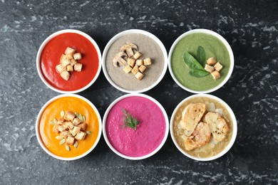 Different tasty cream soups in bowls on black textured table, flat lay