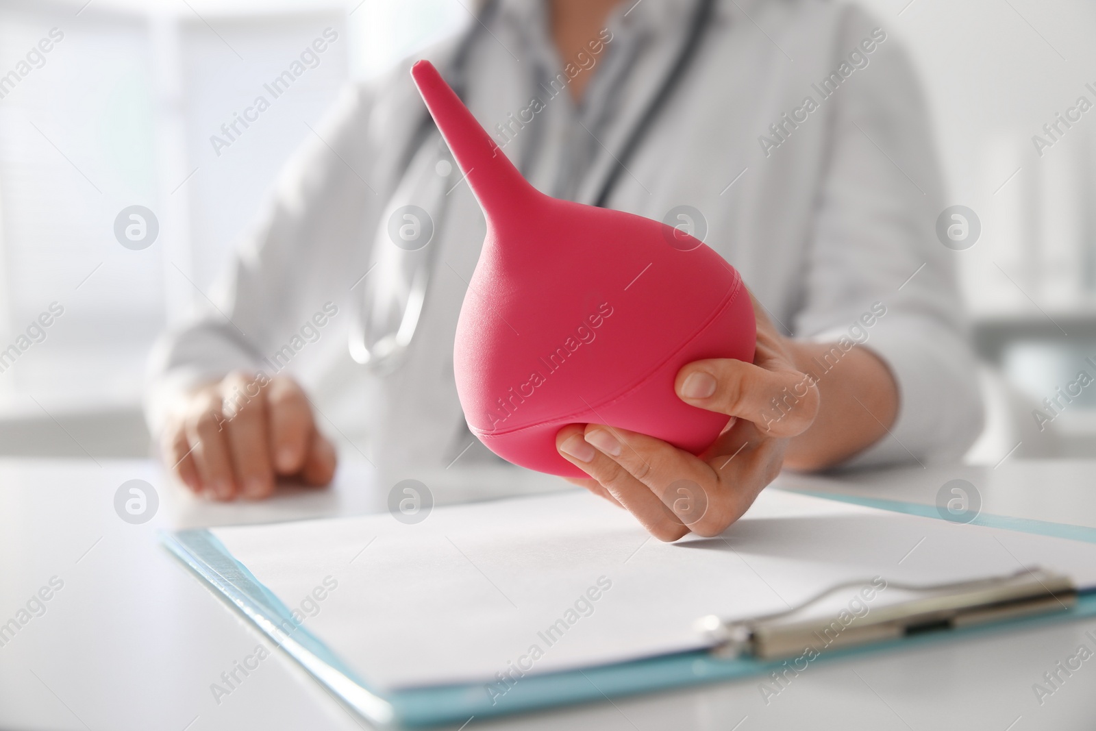 Photo of Doctor holding pink enema at table in hospital, closeup