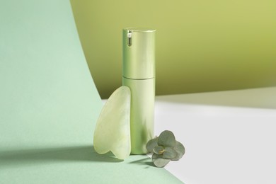 Jade gua sha tool, eucalyptus branch and cosmetic product on color background