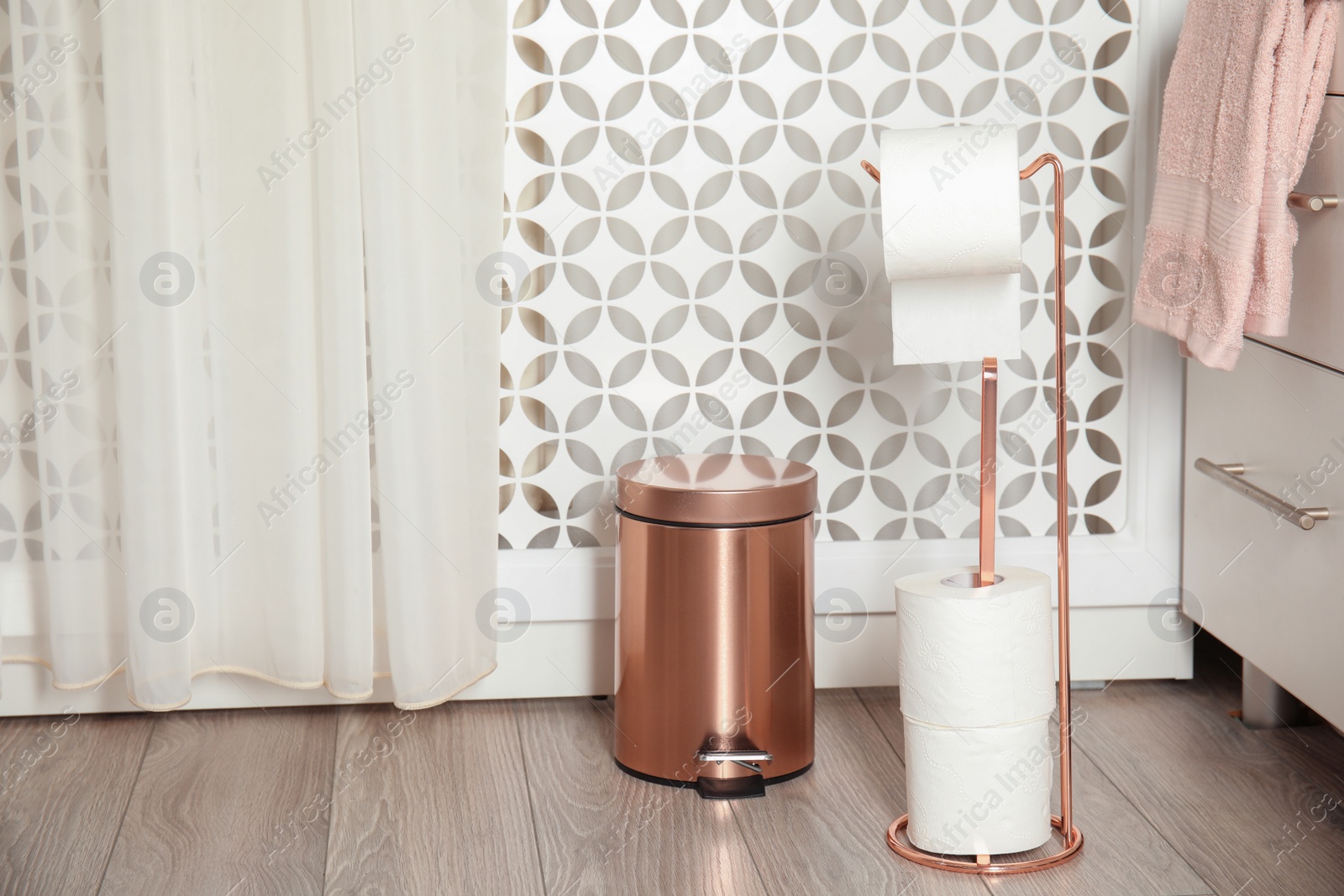 Photo of Toilet paper holder with rolls and trash bin in bathroom interior