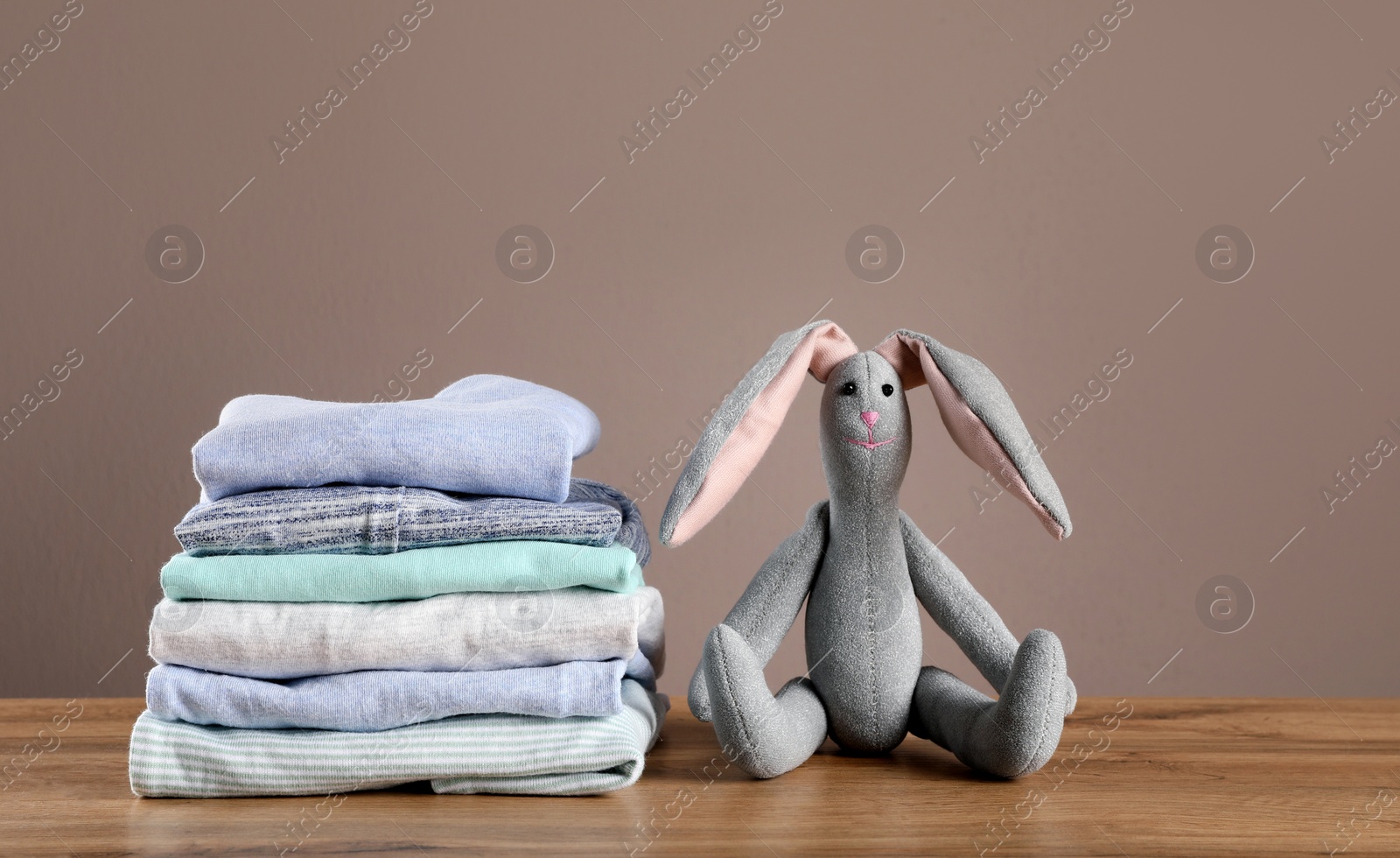 Photo of Stack of baby boy's clothes and toy on wooden table against brown background, space for text