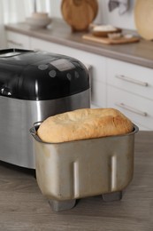 Breadmaker and fresh homemade bread in pan on wooden table in kitchen