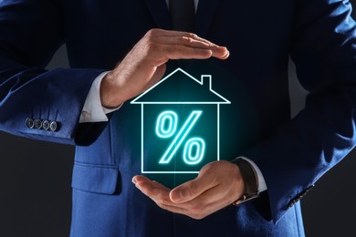 Image of Mortgage. Man holding virtual house with percent sign on black background, closeup