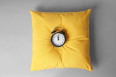 Photo of Soft decorative pillow with alarm clock on light background