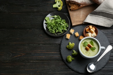 Photo of Flat lay composition with cup of broccoli cream soup on black wooden table, space for text