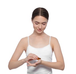 Young woman applying essential oil onto wrist on white background