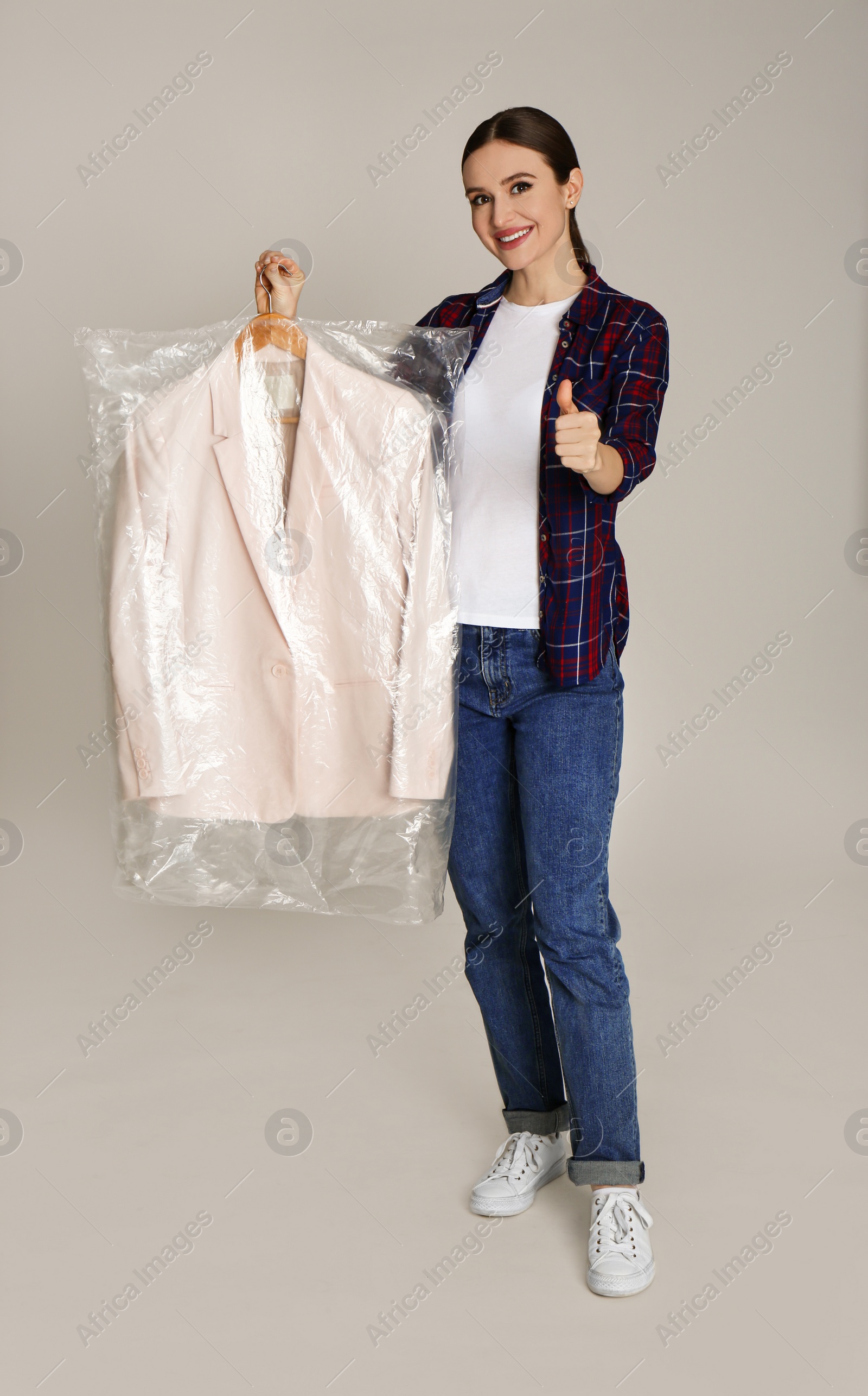 Photo of Young woman holding hanger with jacket on light grey background. Dry-cleaning service