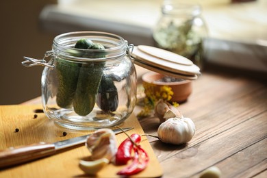 Glass jar with fresh cucumbers and other ingredients on wooden table, space for text. Pickling vegetables