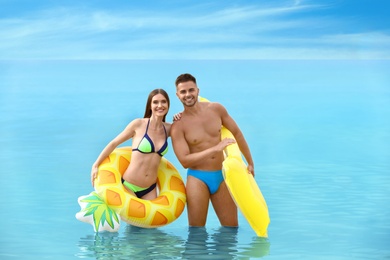 Photo of Young woman in bikini and her boyfriend with inflatable toys on beach. Lovely couple