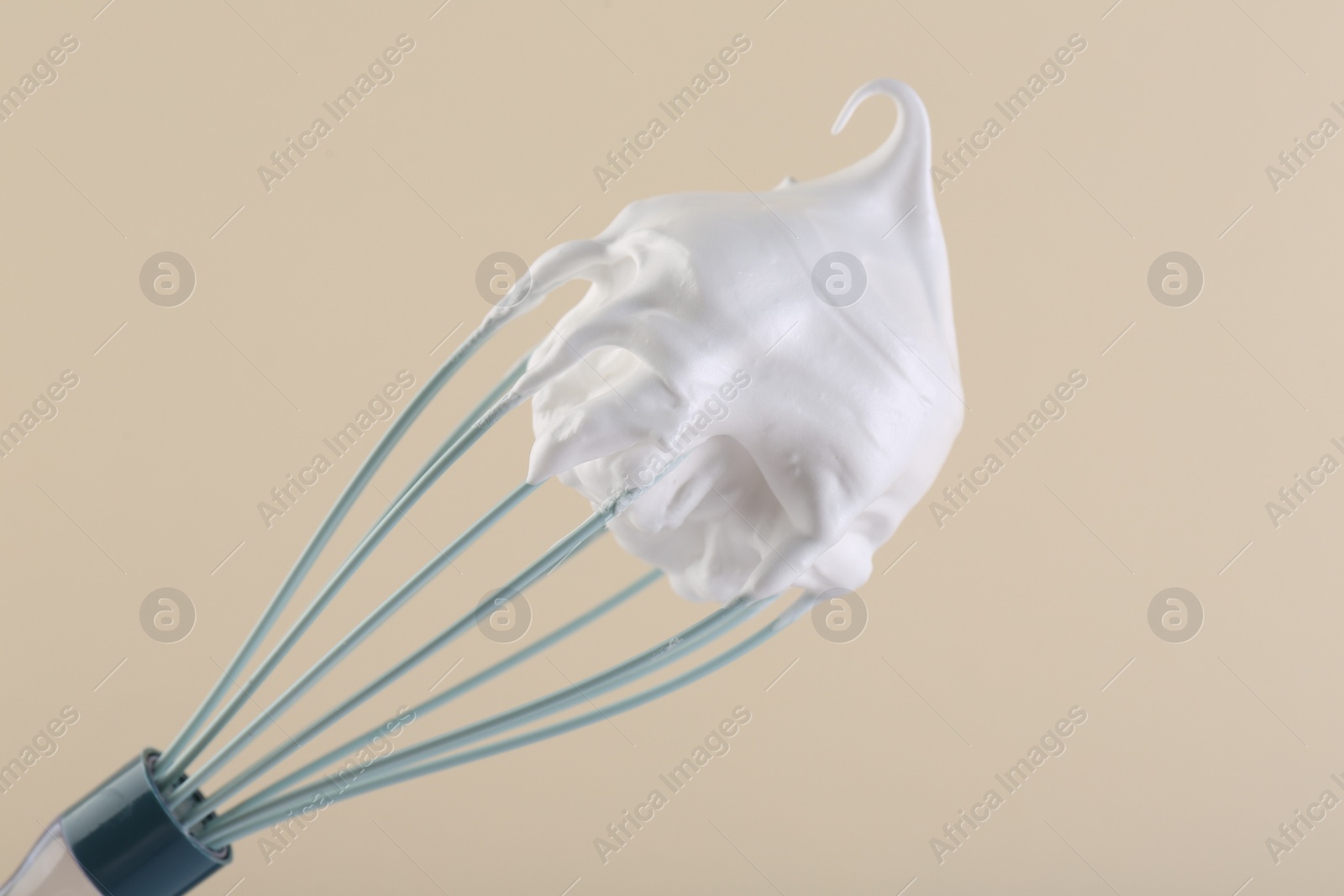 Photo of Whisk with whipped cream on beige background, closeup