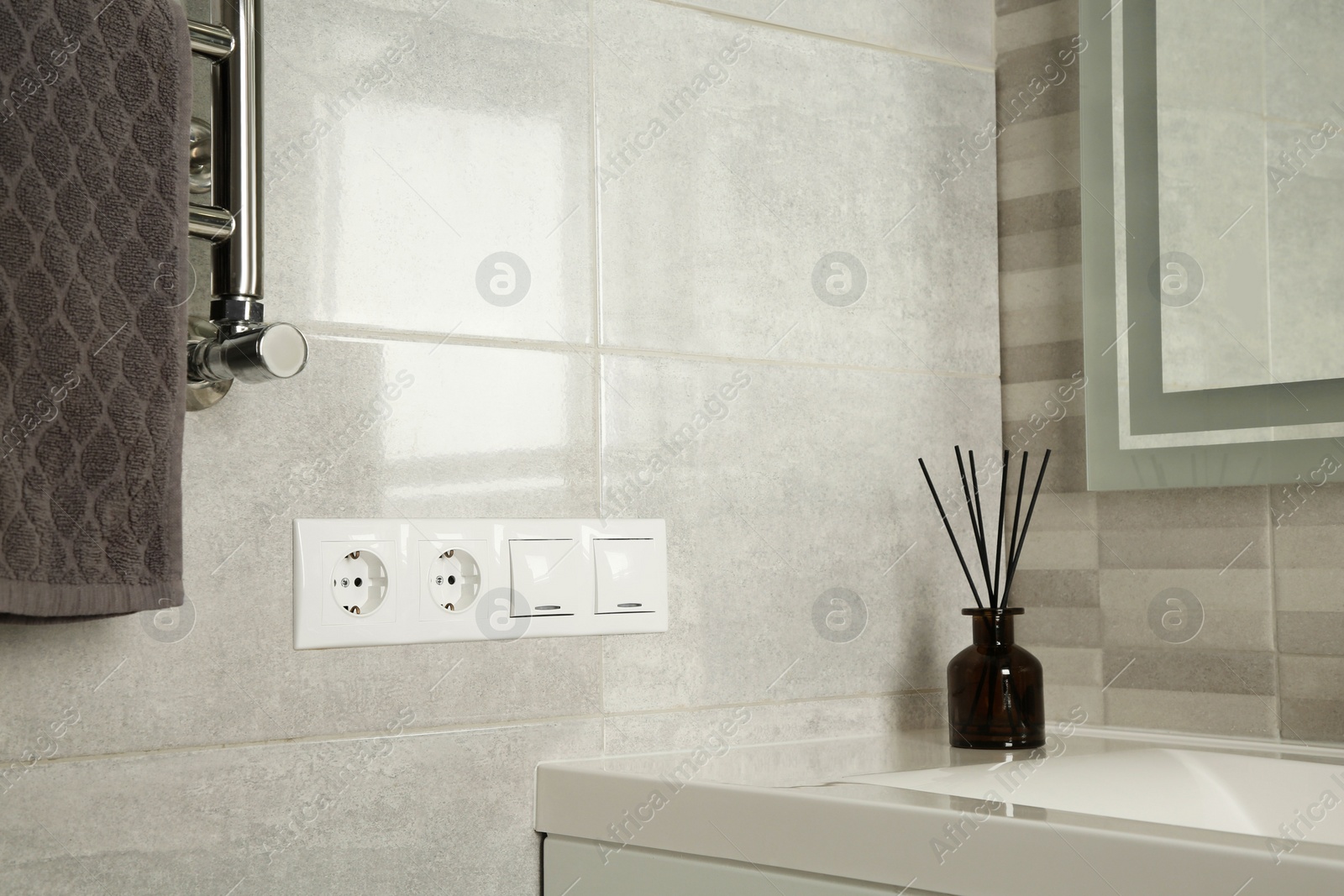 Photo of Light switches and power sockets near heated towel rail on wall in bathroom