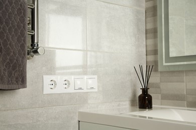Photo of Light switches and power sockets near heated towel rail on wall in bathroom