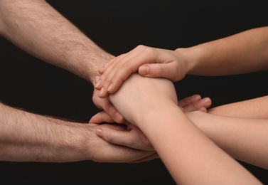 Photo of Young people putting their hands together on dark background, closeup