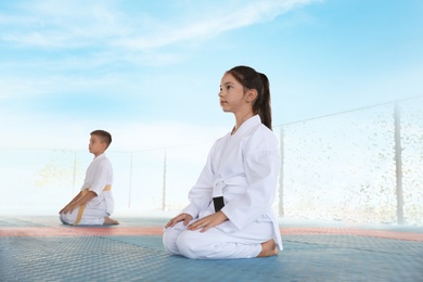 Photo of Children in kimono sitting on tatami outdoors. Karate practice