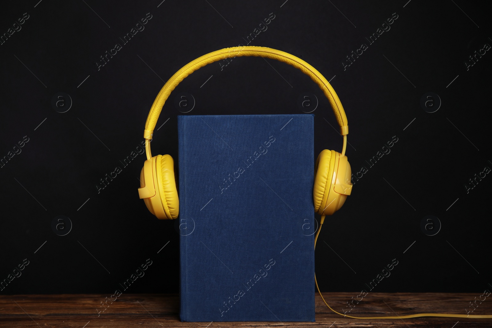 Photo of Book and modern headphones on wooden table against black background