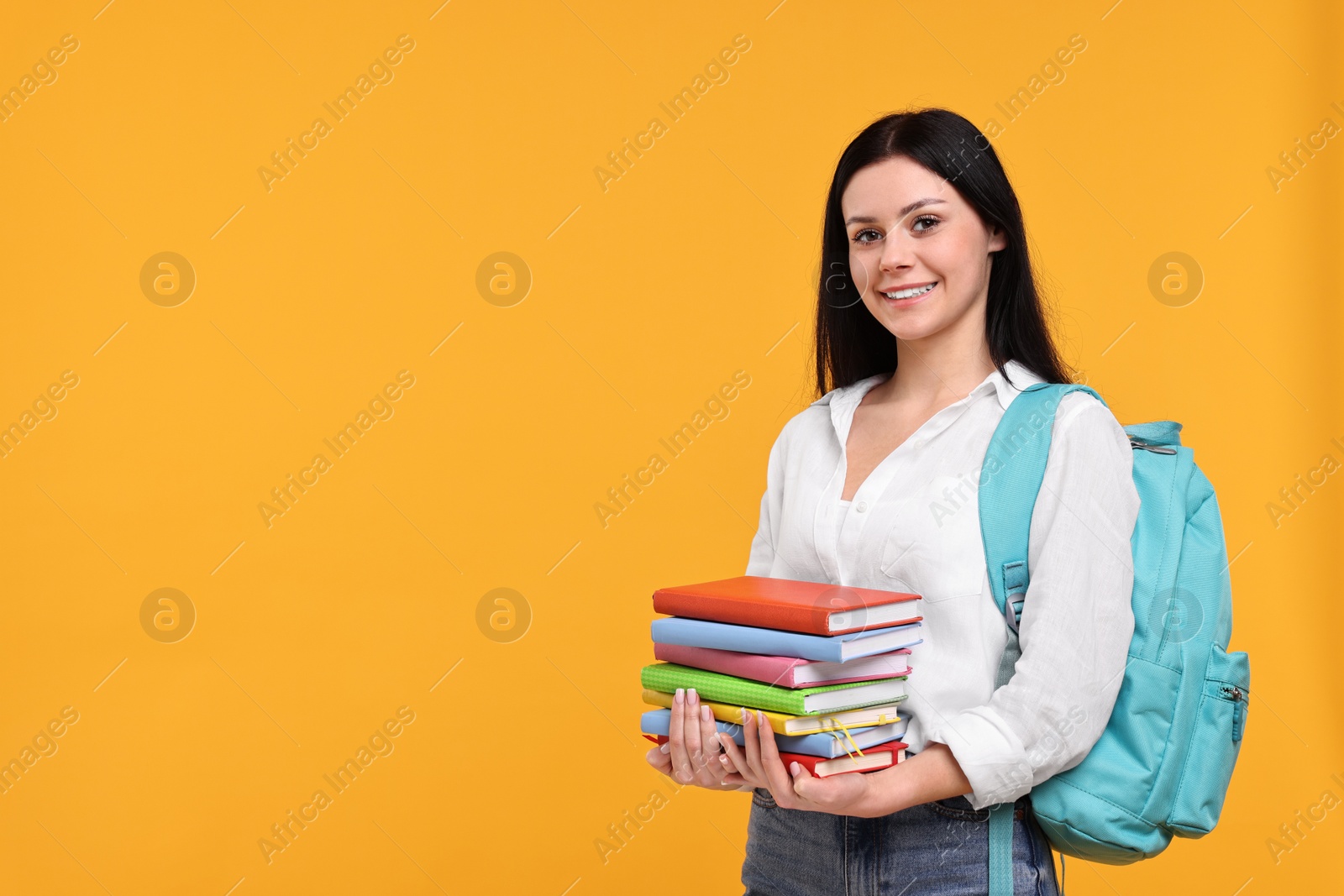Photo of Smiling student with stack of books on yellow background. Space for text