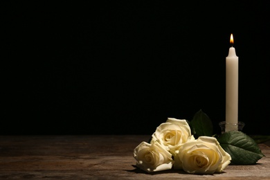 Photo of Beautiful white roses and candle on table against black background. Funeral symbol