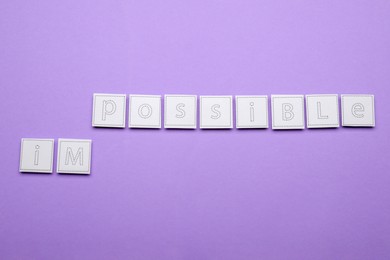 Photo of Motivation concept. Changing word from Impossible into Possible by removing paper with letters on violet background, flat lay
