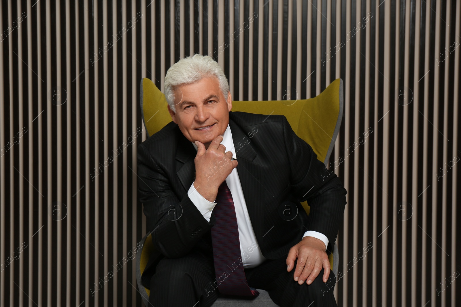 Photo of Happy mature businessman sitting in armchair near wood slat wall