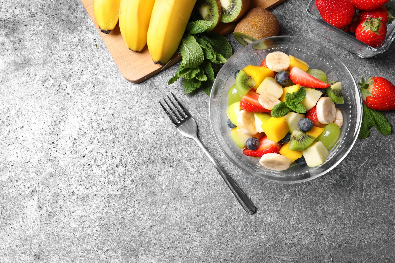 Photo of Delicious fresh fruit salad in bowl on grey table, flat lay. Space for text