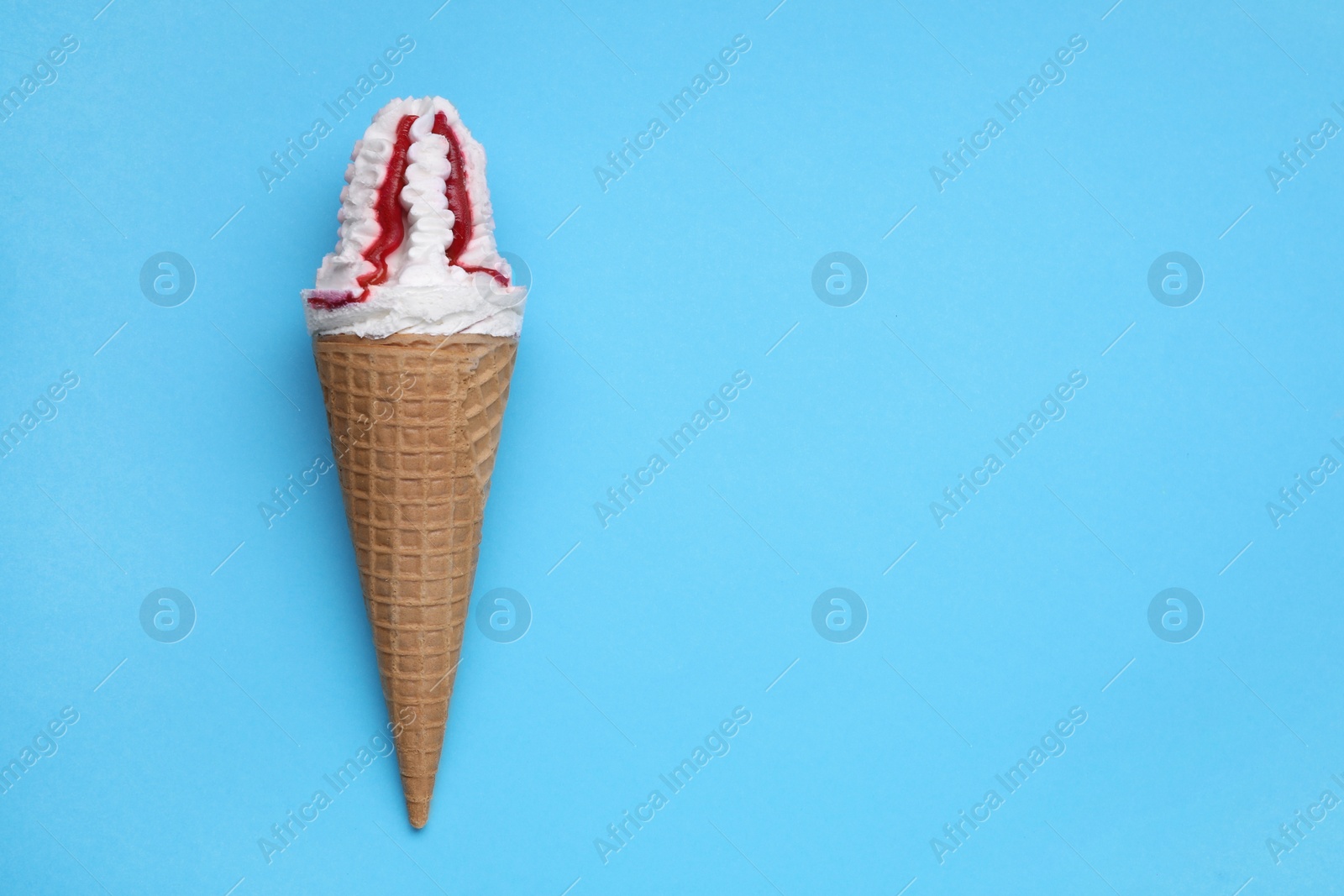 Photo of Delicious ice cream with raspberry jam in waffle cone on light blue background, top view. Space for text