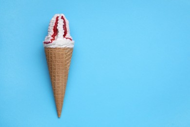 Photo of Delicious ice cream with raspberry jam in waffle cone on light blue background, top view. Space for text