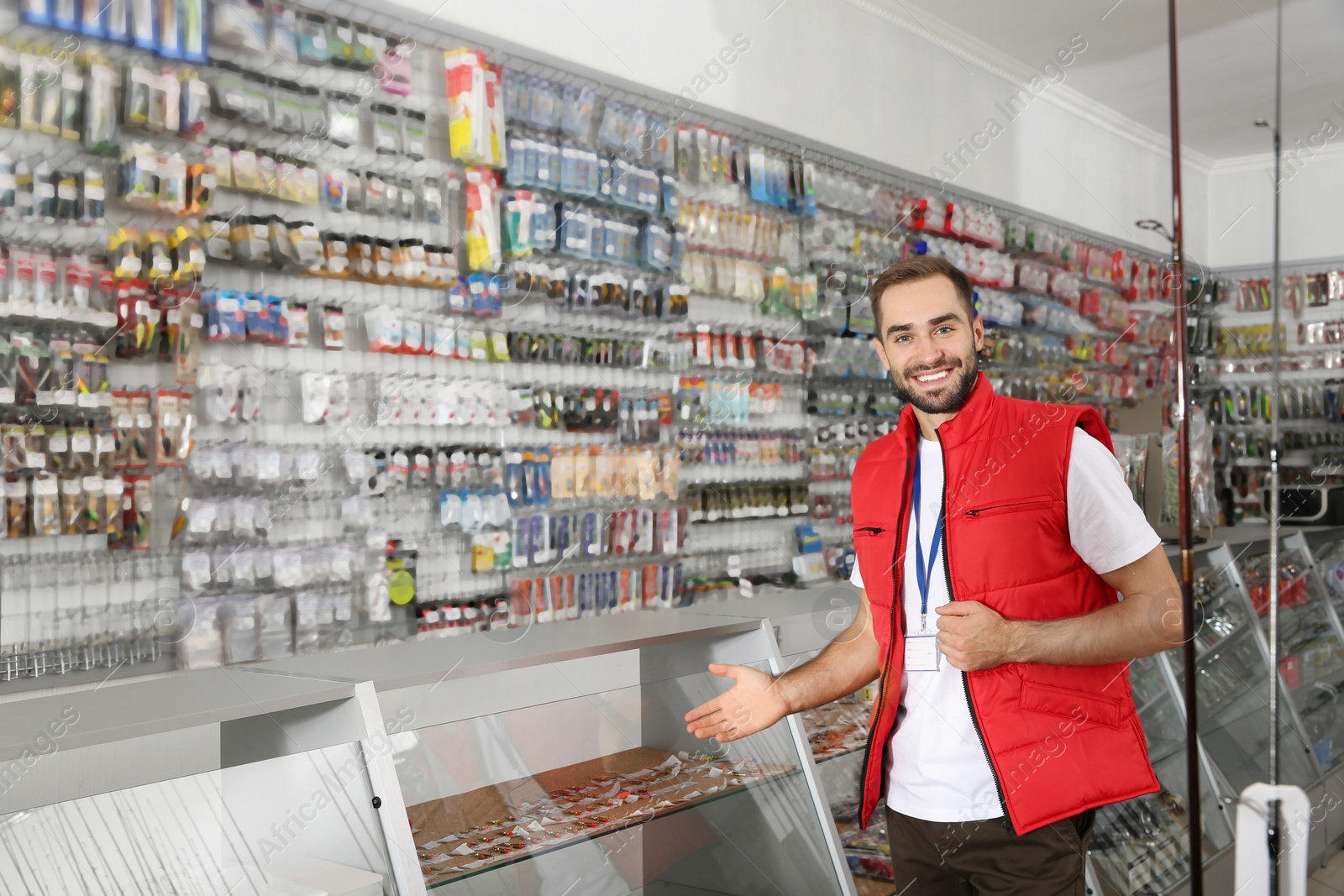 Photo of Salesman standing near showcase with fishing equipment in sports shop. Space for text