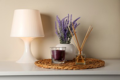 Photo of Aromatic reed air freshener, candle, lamp and lavender flowers on white table indoors