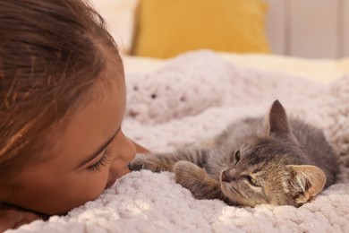 Photo of Cute little girl with kitten on white blanket indoors, closeup. Childhood pet