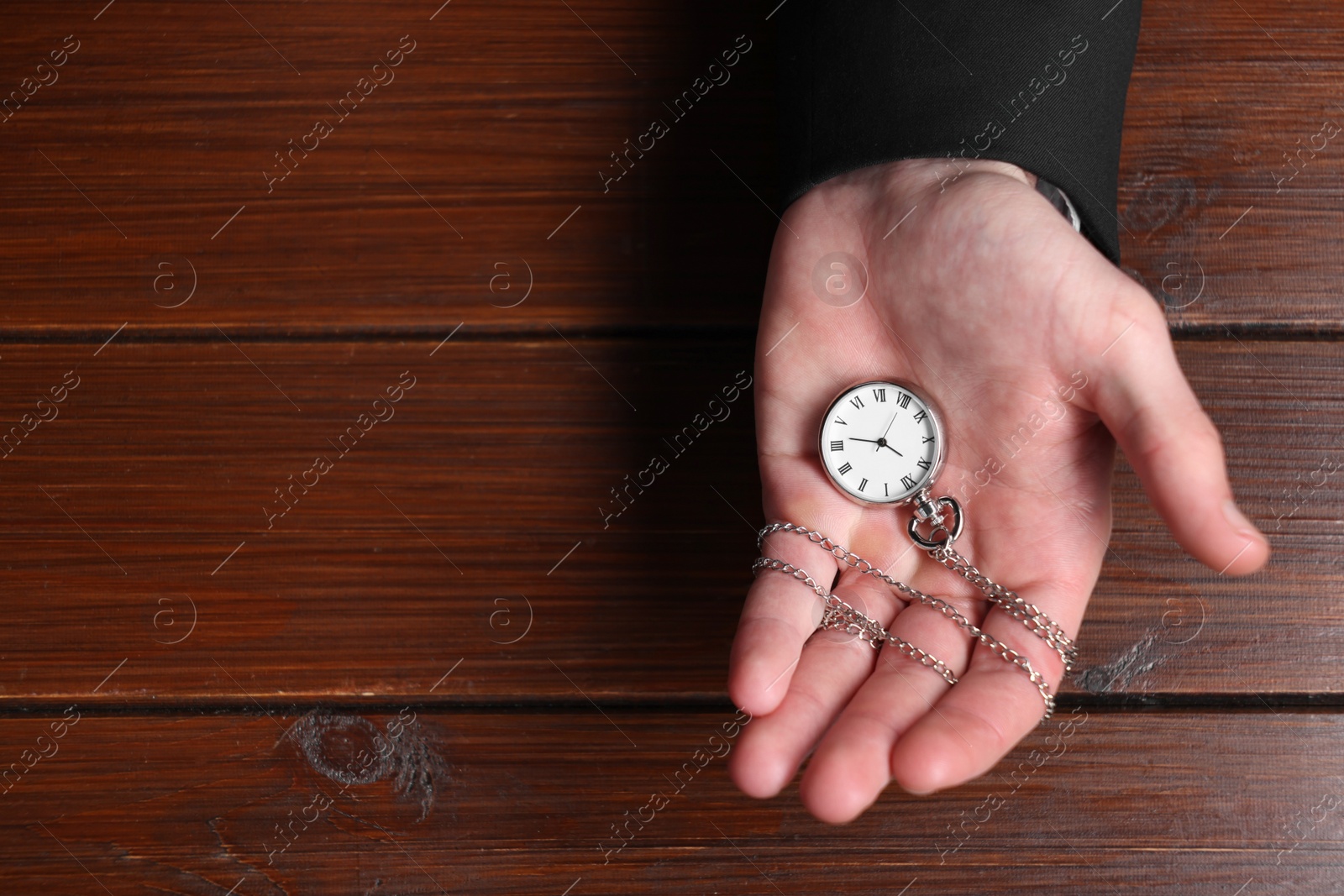 Photo of Man holding chain with elegant pocket watch at wooden table, top view. Space for text