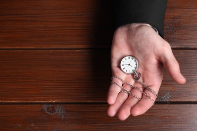 Photo of Man holding chain with elegant pocket watch at wooden table, top view. Space for text