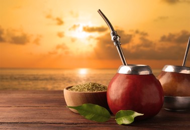 Image of Calabashes with mate tea and bombilla on wooden table outdoors at sunset. Space for text