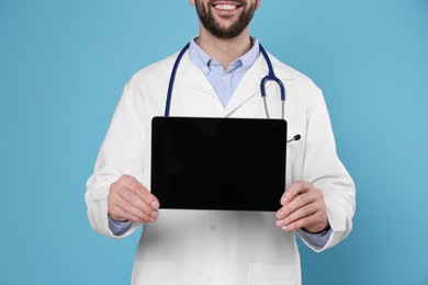 Photo of Closeup view of doctor with stethoscope and blank tablet on light blue background, space for design. Cardiology concept