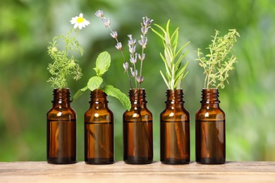 Bottles with essential oils and plants on wooden table against blurred green background