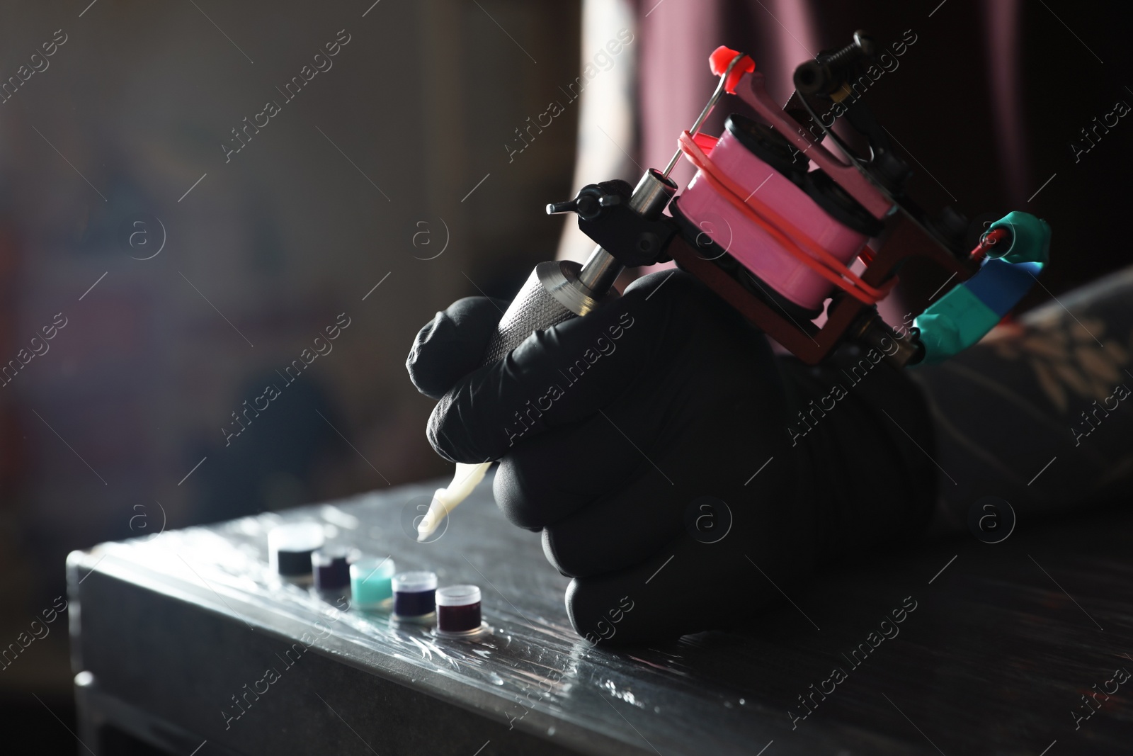 Photo of Tattoo artist with machine and ink at wooden table, closeup