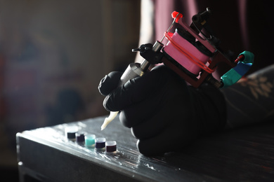 Photo of Tattoo artist with machine and ink at wooden table, closeup